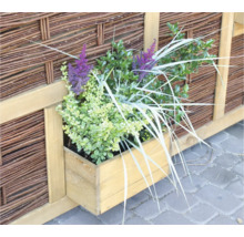 Bac à fleurs en bois avec des plantes devant une clôture tressée