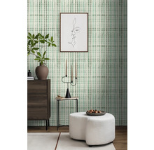 Wohnraum mit gemusterter Tapete, Kommode, Beistelltisch und Ottomane.