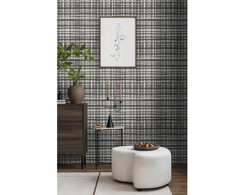 Wohnraum mit gemusterter Tapete, Kommode, Beistelltisch, Kerzenständer und Hocker.