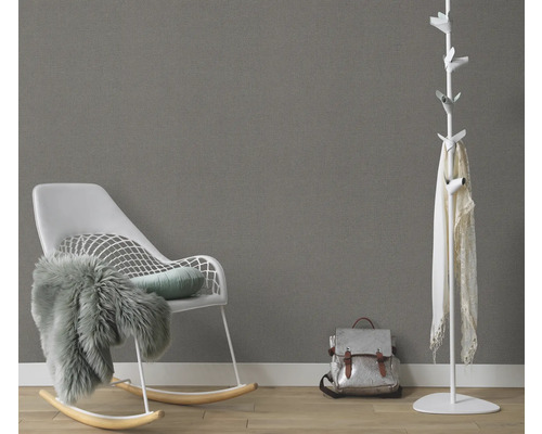 Salon avec fauteuil à bascule, porte-manteau et sac à dos devant un mur gris