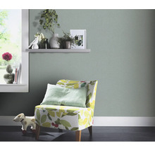 Wohnraum mit hellgrüner Tapete, Sessel mit Blätterdesign und Dekorationen auf einem Regal