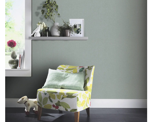 Wohnraum mit hellgrüner Tapete, Sessel mit Blätterdesign und Dekorationen auf einem Regal