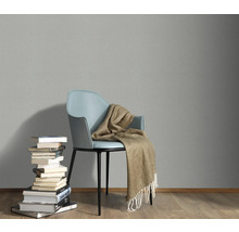 Szene mit einem Stuhl, einer Decke und einem Bücherstapel vor einer grauen Wand.