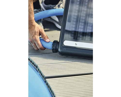 Une personne raccorde un tuyau bleu à un absorbeur solaire.