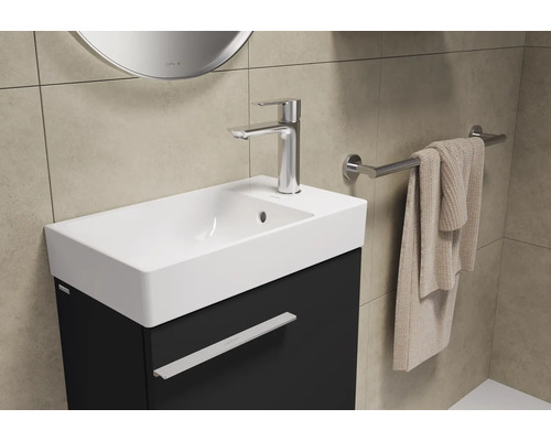 Lavabo de salle de bain avec robinet, serviette et porte-serviettes devant un mur carrelé