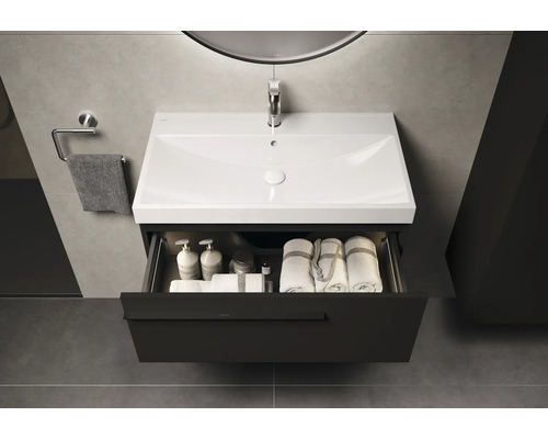 Meuble-lavabo avec tiroir ouvert, rempli de serviettes et de produits de soins dans la salle de bain.