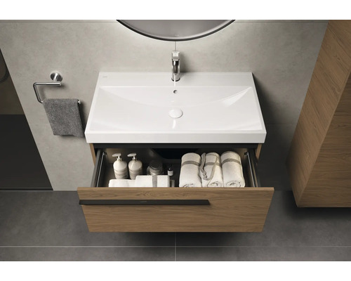 Meuble sous-vasque avec tiroir ouvert, lavabo, serviettes et produits de soin dans une salle de bains moderne