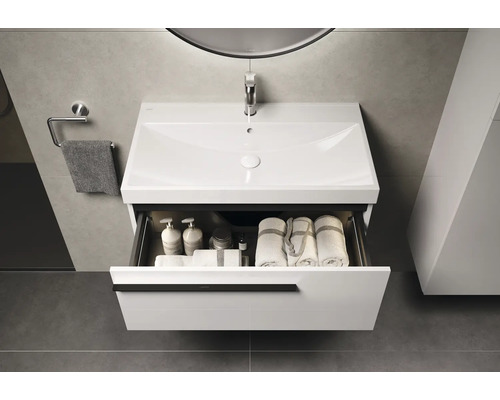 Meuble sous-lavabo avec tiroir ouvert, contenant des serviettes et des produits de soin