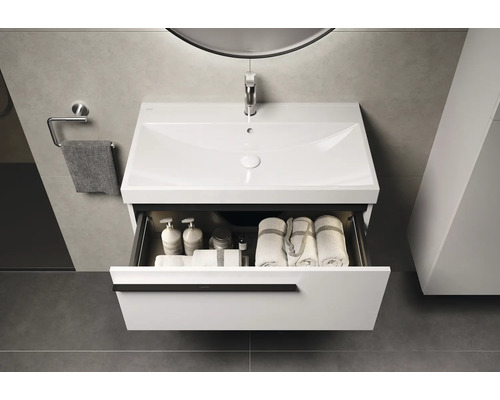 Meuble-lavabo avec tiroir ouvert, serviettes et produits de soins dans la salle de bains.