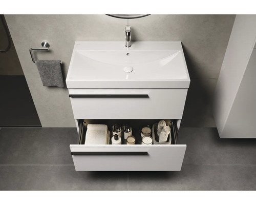 Salle de bains moderne avec meuble sous-lavabo blanc et tiroir ouvert, rempli de serviettes et d'accessoires de bain.