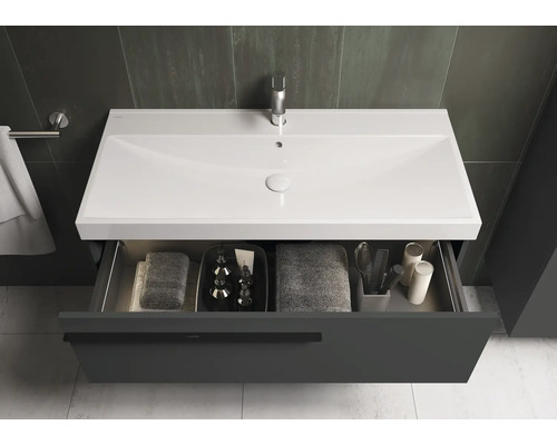 Meuble-lavabo avec tiroir ouvert contenant des serviettes et des articles de toilette