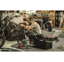 Zwei Männer reparieren ein Motorrad mit einem Werkzeugkasten in einer Garage.