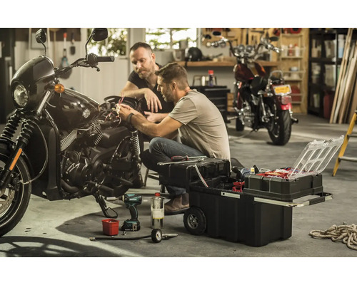 Zwei Männer reparieren ein Motorrad mit einem Werkzeugkasten in einer Garage.
