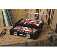 Geöffnete, schwarze Pattfield Sortimentsbox mit transparentem Deckel und diversen Schrauben, Nägeln und Dübeln auf einem Holztisch.