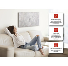 Frau entspannt sich auf dem Sofa unter einer Wandheizung mit Marmor-Optik. Wartungsfrei, einfache Installation und Smart Home fähig.