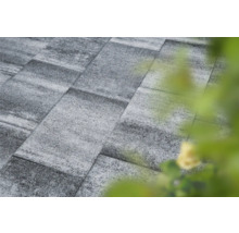 Graue Pflastersteine bilden eine Gartenfläche.