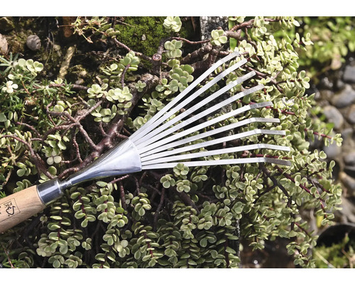 Balai à feuilles en métal avec manche en bois devant des plantes vertes