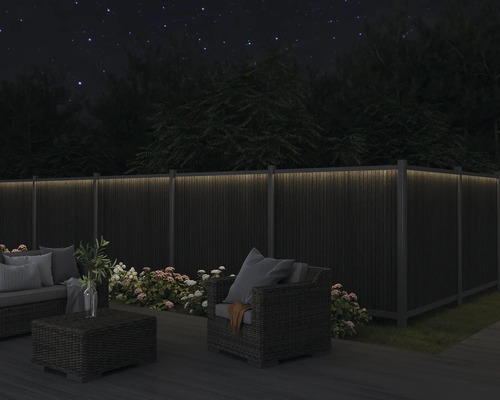 Gartenmöbel auf einer Terrasse mit beleuchtetem Zaun im Dunkeln