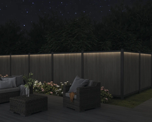 Szene mit beleuchtetem Gartenzaun, Sitzgruppe und Bepflanzung bei Nacht