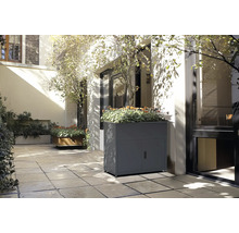 Scène avec un bac à fleurs gris avec des portes et des plantes sur une terrasse.