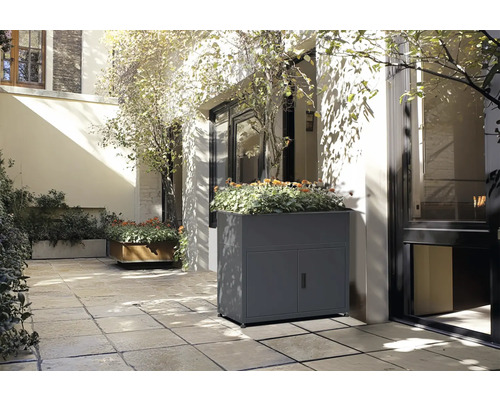 Scène avec un bac à fleurs gris avec des portes et des plantes sur une terrasse.