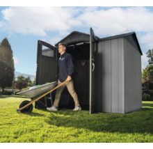 Mann schiebt Schubkarre aus einem Geräteschuppen im Garten