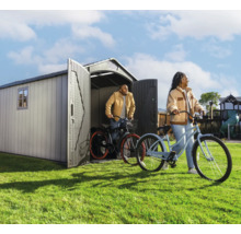 Gartenszene mit Gerätehaus und zwei Personen mit Fahrrädern auf dem Rasen