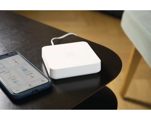 Smart Home System mit Smartphone-App und Zentraleinheit auf einem Tisch.