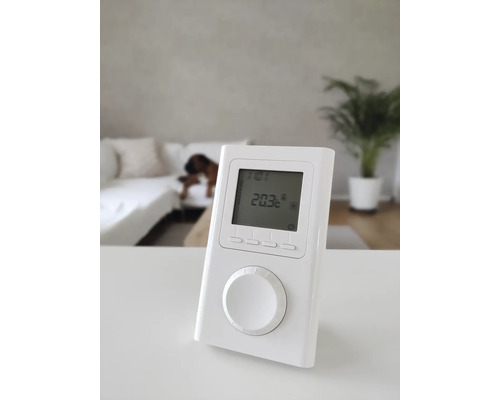 Weißer elektronischer Raumthermostat mit digitaler Anzeige auf einem Tisch