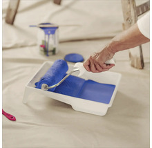 Une personne remplit un bac à peinture avec un rouleau à peinture avec de la peinture pour peindre.