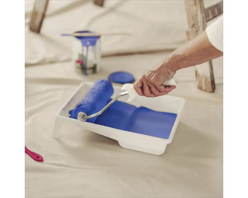 Une personne remplit un bac à peinture avec un rouleau à peinture avec de la peinture pour peindre.