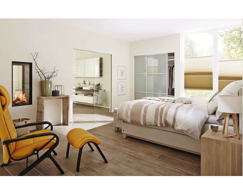 Chambre lumineuse avec lit double, fauteuil, cheminée et vue sur la salle de bain à travers une porte vitrée