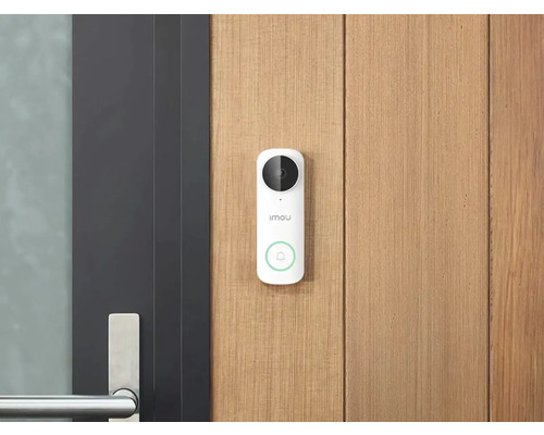 Sonnette vidéo Imou blanche avec caméra et bouton d'appel sur un mur en bois clair à côté d'une porte sombre moderne avec poignée en métal.