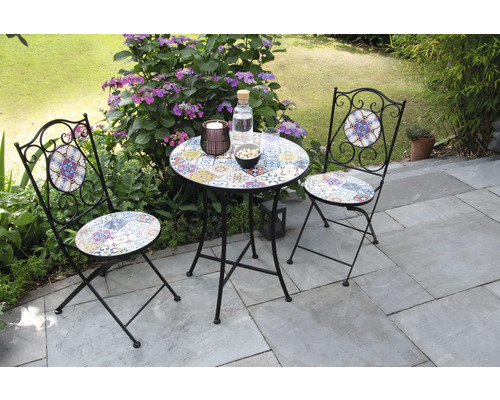 Scène de jardin avec une petite table et deux chaises à motifs mosaïque sur une terrasse.