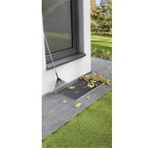 Lichtschachtabdeckung mit Laub und Rechen am Haus