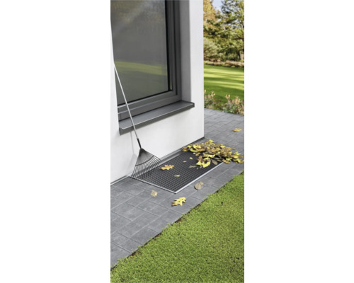 Lichtschachtabdeckung mit Laub und Rechen am Haus