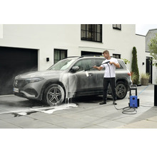 Mann wäscht Auto mit Hochdruckreiniger vor einem Haus.