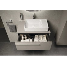Meuble-lavabo de salle de bains avec tiroir ouvert, avec des serviettes et des accessoires de bain, au-dessus du meuble-lavabo se trouve un lavabo rectangulaire