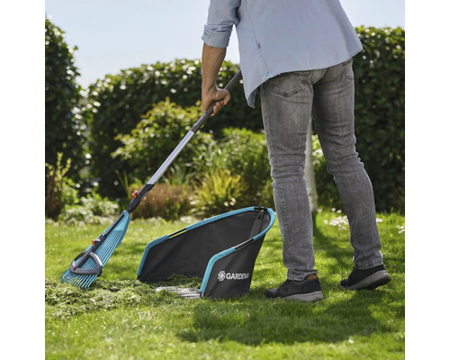 Gartenszene mit Gärtner beim Rasenkehren mit einem Fächerbesen und Rasensammler von Gardena