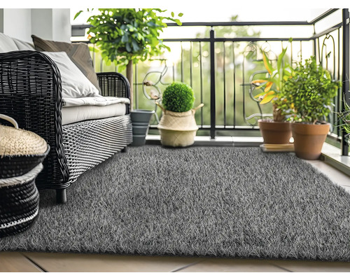 Scène de balcon avec canapé en rotin, plantes et gazon synthétique gris