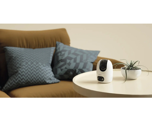 Caméra de surveillance Imou sur une table à côté d'une plante d'intérieur et d'un canapé