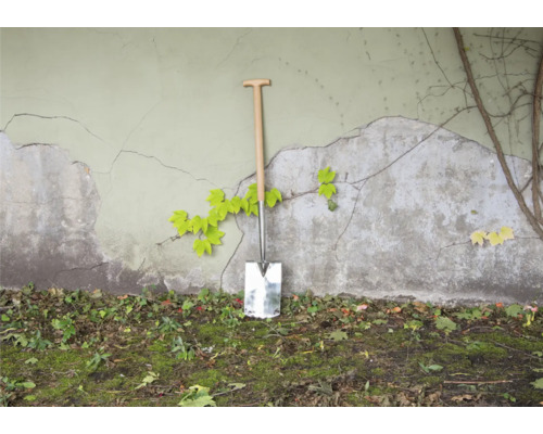 Bêche avec manche en bois contre un mur