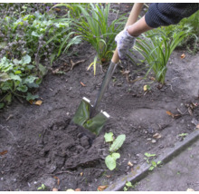 Une personne utilise une bêche pour creuser dans le jardin.