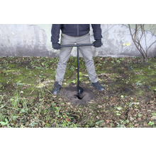 Une personne utilise une tarière pour percer un trou dans le sol.