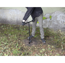 Une personne perce un trou dans le sol avec une tarière.