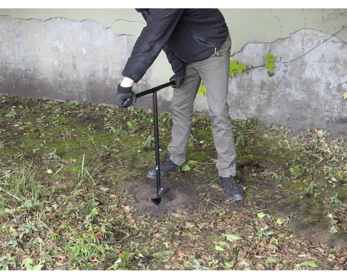 Une personne perce un trou dans le sol avec une tarière.