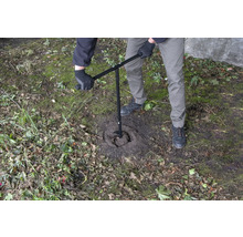Une personne utilise une tarière pour percer un trou dans le sol.