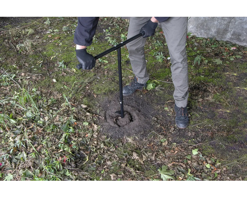 Une personne utilise une tarière pour percer un trou dans le sol.