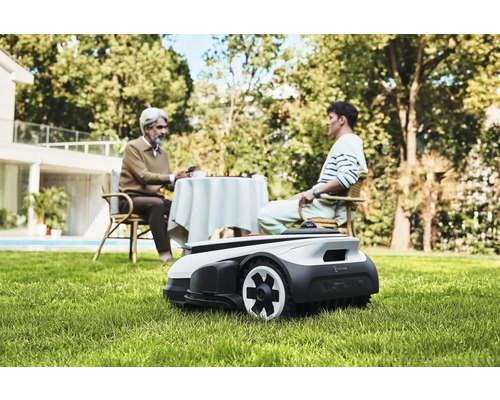 Scène avec un robot tondeuse à gazon dans le jardin, tandis que deux personnes sont assises à une table