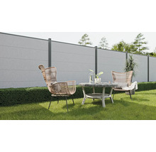 Scène de jardin avec clôture en béton, fauteuils en rotin et table ronde sur une pelouse.